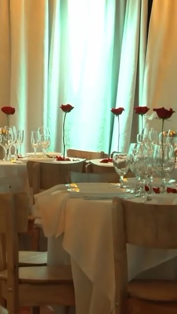 Mesas tendidas con rosas rojas frente a las cortinas del salón.