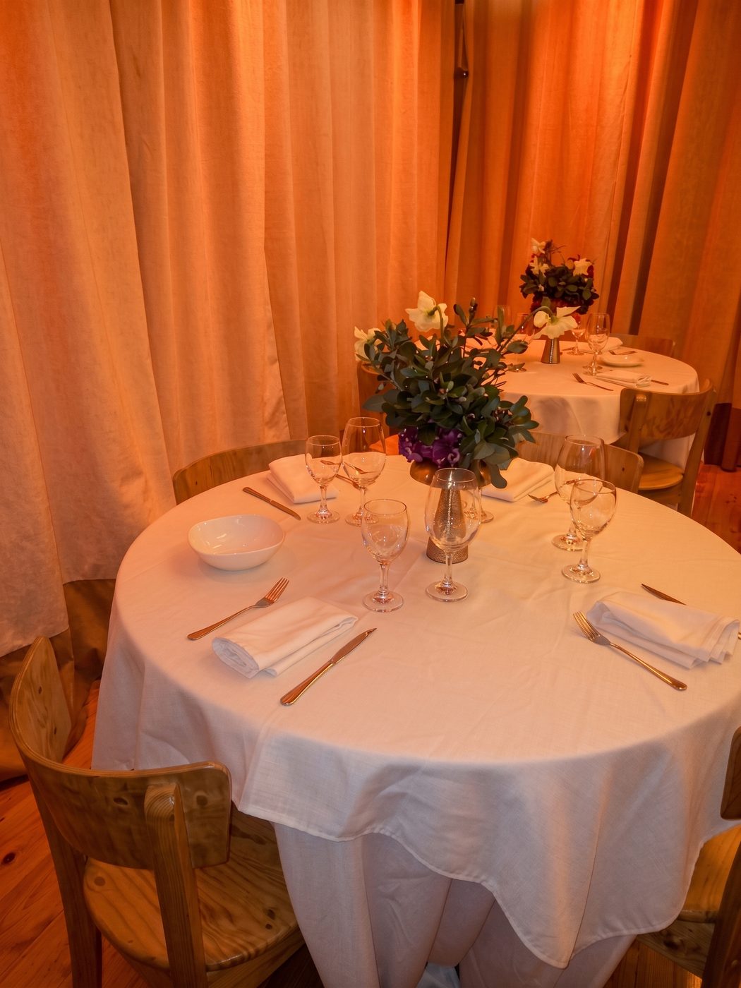 Mesa vestida con mantel blanco, copas y centro floral.